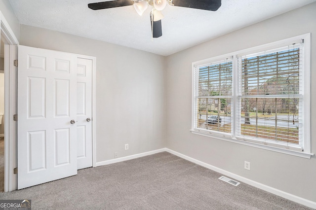 unfurnished bedroom with a ceiling fan, baseboards, visible vents, carpet floors, and a textured ceiling