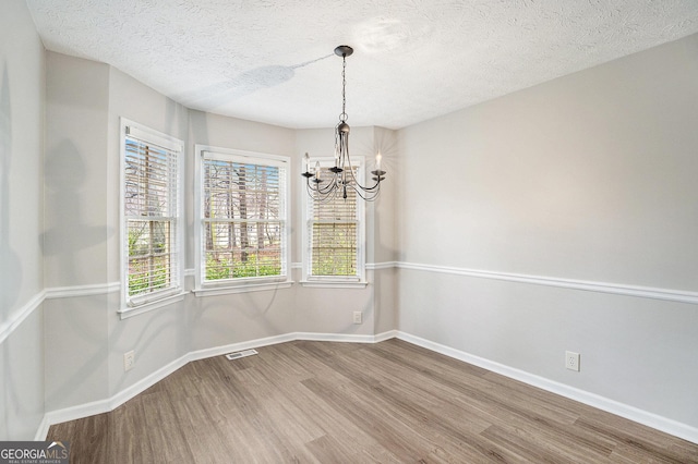 unfurnished dining area with wood finished floors, visible vents, baseboards, a textured ceiling, and a notable chandelier