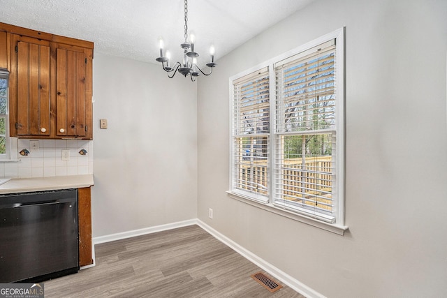 unfurnished dining area featuring light wood finished floors, visible vents, baseboards, a chandelier, and a textured ceiling