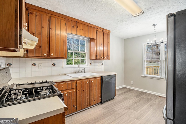 kitchen featuring under cabinet range hood, light wood-type flooring, brown cabinetry, stainless steel appliances, and a sink