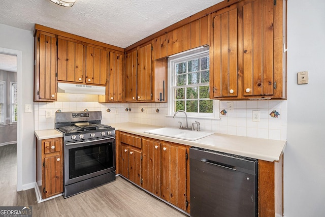 kitchen featuring under cabinet range hood, light wood-style floors, brown cabinetry, stainless steel appliances, and a sink