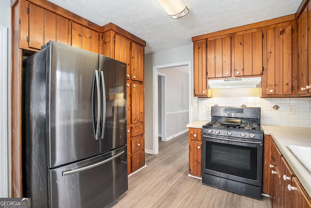 kitchen with under cabinet range hood, appliances with stainless steel finishes, brown cabinetry, and light countertops