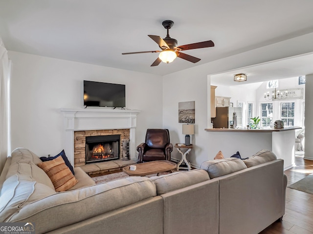 living area featuring a stone fireplace, ceiling fan with notable chandelier, and wood finished floors