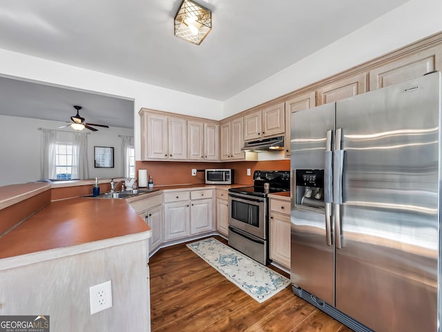 kitchen with dark wood-style floors, a peninsula, a sink, stainless steel appliances, and under cabinet range hood