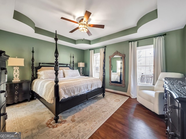 bedroom featuring a tray ceiling, multiple windows, wood finished floors, and baseboards