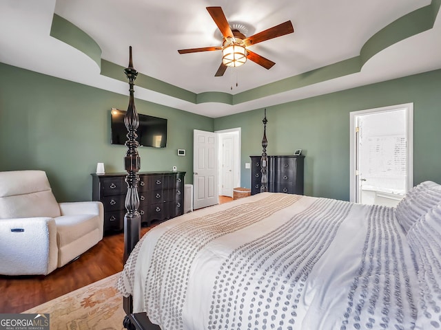 bedroom featuring ensuite bath, a raised ceiling, a ceiling fan, and wood finished floors