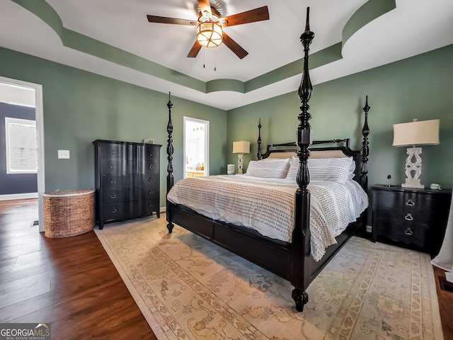 bedroom featuring baseboards, a raised ceiling, wood finished floors, and a ceiling fan