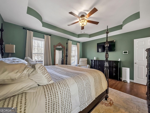 bedroom featuring a tray ceiling, multiple windows, wood finished floors, and ceiling fan