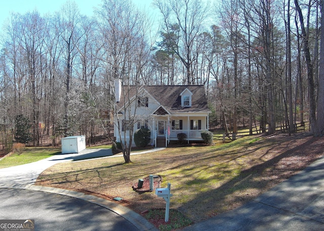 cape cod home with an outbuilding, a porch, driveway, and a front yard