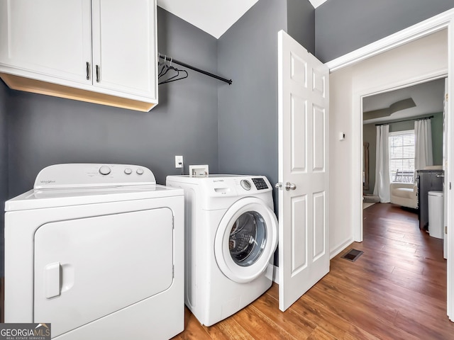 laundry room featuring washer and dryer, visible vents, cabinet space, and wood finished floors