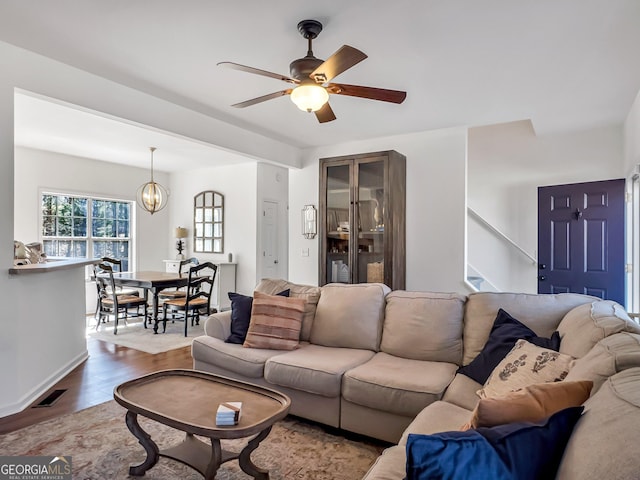 living area with ceiling fan with notable chandelier, stairway, wood finished floors, and visible vents