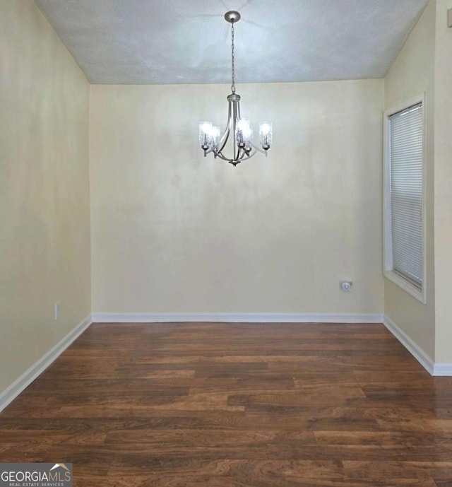 spare room featuring baseboards, an inviting chandelier, and dark wood-style flooring