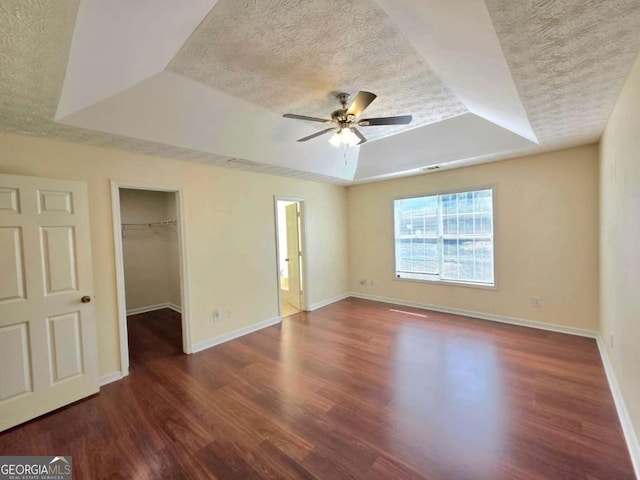 unfurnished bedroom with a tray ceiling, baseboards, a textured ceiling, and wood finished floors