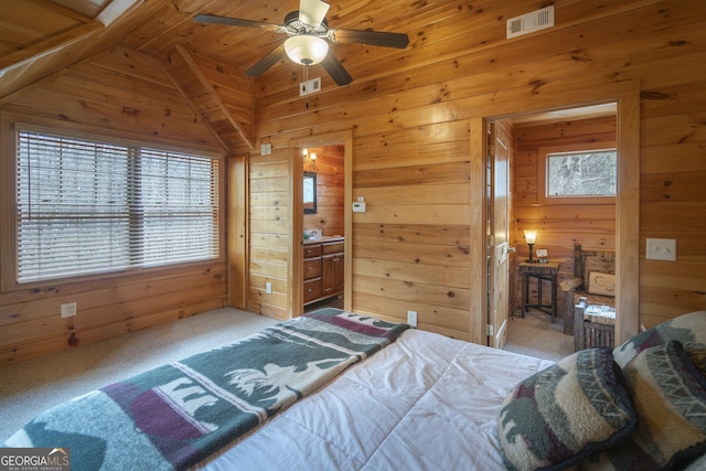 bedroom with visible vents, wooden walls, carpet, vaulted ceiling, and ensuite bathroom