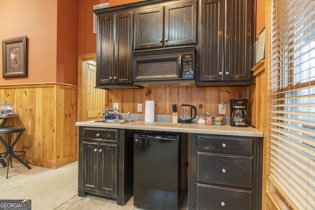 kitchen with a wainscoted wall, a sink, black appliances, light countertops, and wood walls