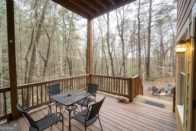 wooden deck with a view of trees, a fire pit, and outdoor dining space