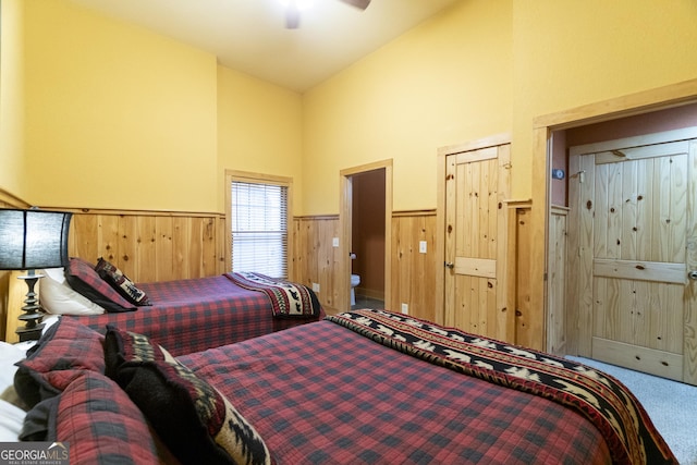 bedroom with a wainscoted wall, wood walls, high vaulted ceiling, and carpet floors