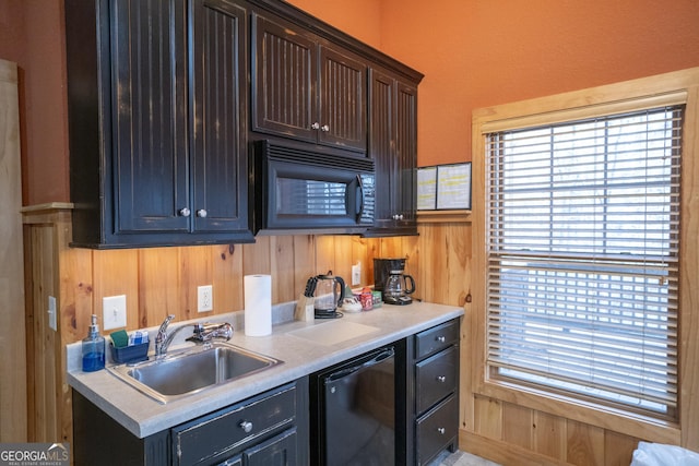 kitchen featuring wood walls, black appliances, light countertops, and a sink