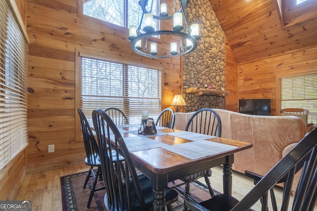 dining room featuring light wood finished floors, wooden walls, a healthy amount of sunlight, and high vaulted ceiling