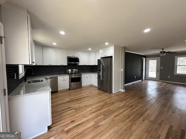 kitchen featuring open floor plan, light stone counters, decorative backsplash, stainless steel appliances, and a sink