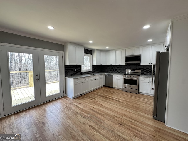 kitchen featuring light wood finished floors, a sink, decorative backsplash, appliances with stainless steel finishes, and white cabinetry