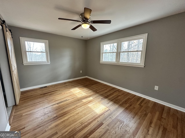 unfurnished bedroom featuring a barn door, baseboards, wood finished floors, and a ceiling fan