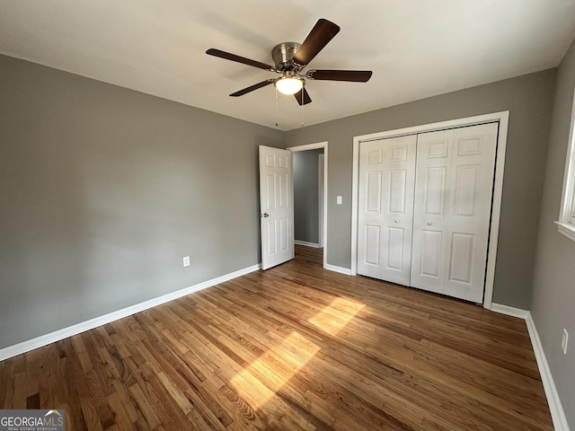 unfurnished bedroom featuring wood finished floors, baseboards, a closet, and ceiling fan