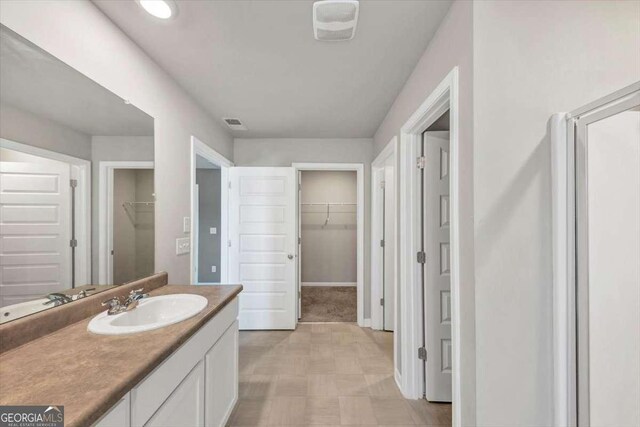 bathroom featuring a walk in closet, baseboards, visible vents, and vanity