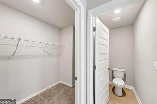 bathroom with recessed lighting, a walk in closet, baseboards, and toilet