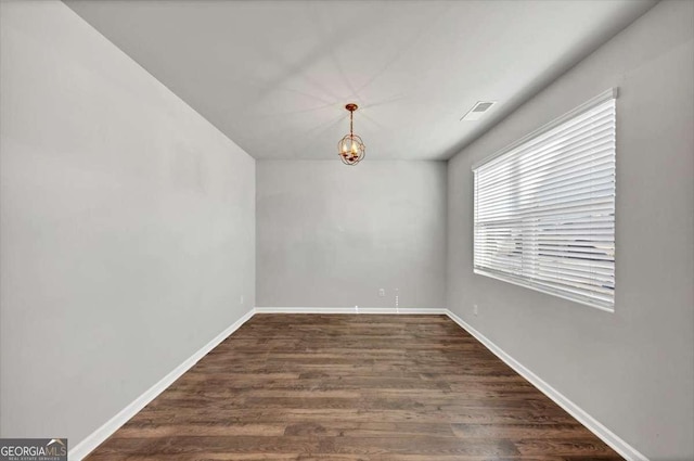 empty room with dark wood finished floors, a chandelier, visible vents, and baseboards