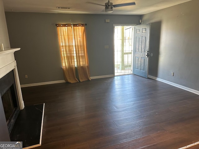 unfurnished living room with visible vents, a fireplace with raised hearth, baseboards, ceiling fan, and dark wood-style floors