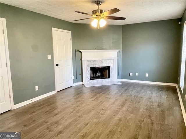 unfurnished living room featuring wood finished floors, baseboards, a fireplace, ceiling fan, and a textured ceiling