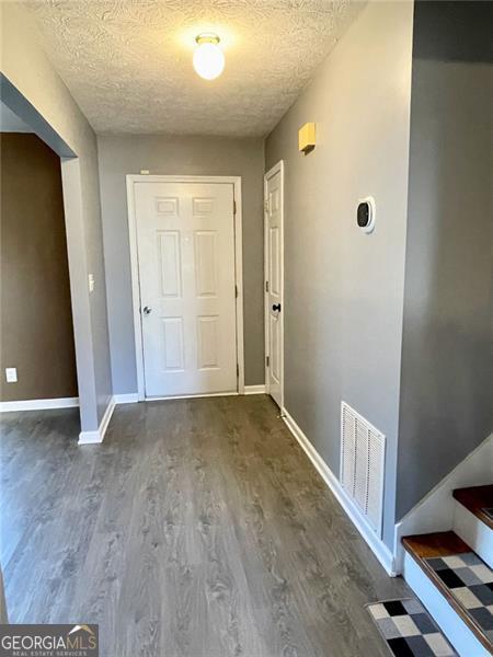 corridor with visible vents, baseboards, a textured ceiling, and wood finished floors