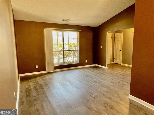 spare room featuring vaulted ceiling, visible vents, baseboards, and wood finished floors