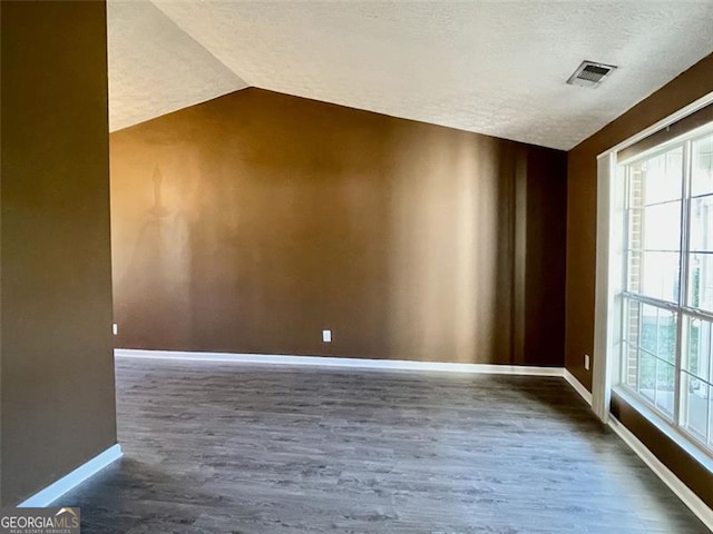 unfurnished room with wood finished floors, visible vents, baseboards, lofted ceiling, and a textured ceiling