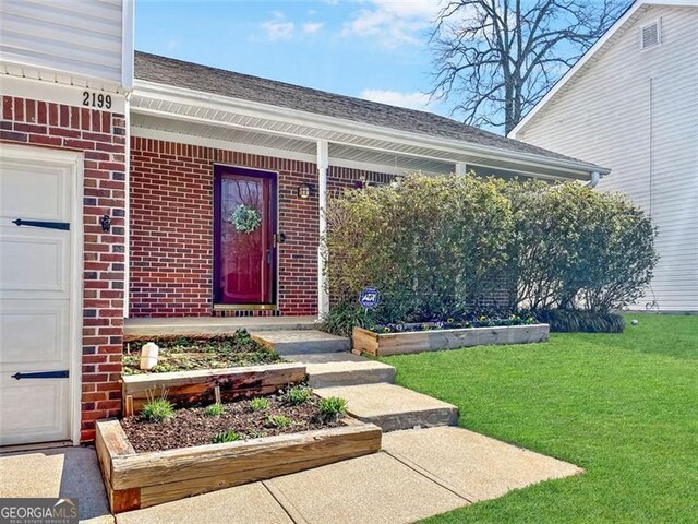 entrance to property featuring brick siding, a garage, a yard, and roof with shingles