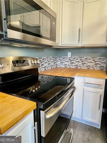 kitchen featuring backsplash, white cabinetry, stainless steel appliances, and wood counters