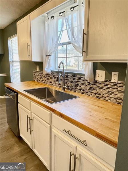 kitchen with dishwashing machine, white cabinetry, wood counters, and a sink