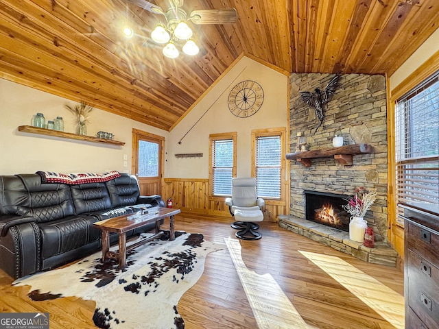 living room with wood-type flooring, a stone fireplace, wooden ceiling, and wainscoting