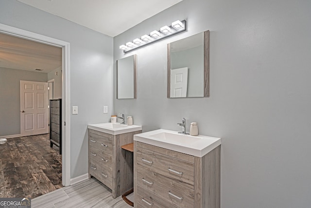 full bath with two vanities, wood finished floors, baseboards, and a sink