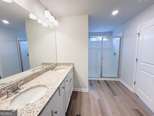 bathroom featuring double vanity, a stall shower, wood finished floors, and a sink