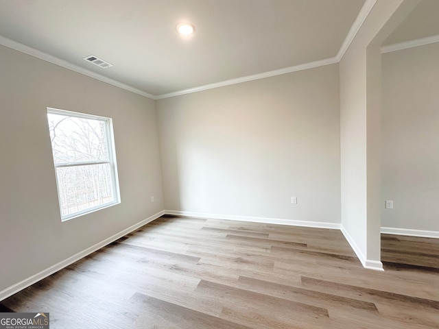 spare room with crown molding, wood finished floors, visible vents, and baseboards