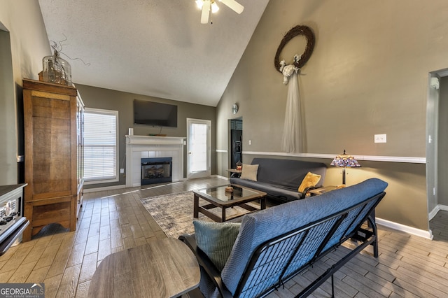 living area featuring wood finish floors, high vaulted ceiling, baseboards, ceiling fan, and a tile fireplace