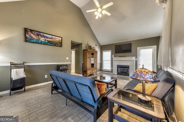 living room featuring wood finished floors, baseboards, high vaulted ceiling, ceiling fan, and a tile fireplace