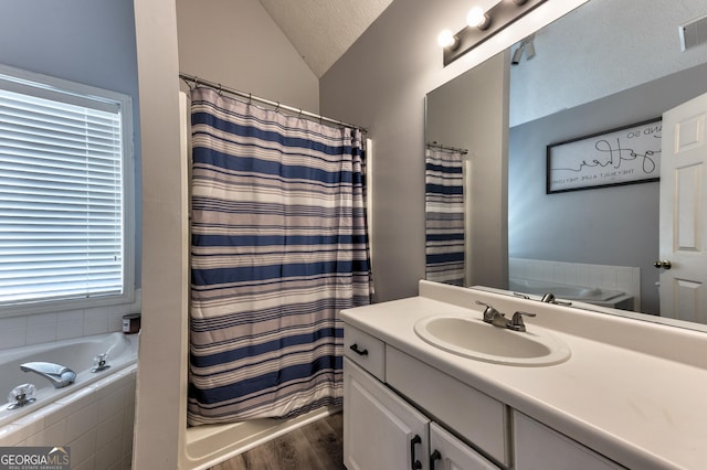 bathroom featuring a textured ceiling, wood finished floors, a relaxing tiled tub, lofted ceiling, and vanity