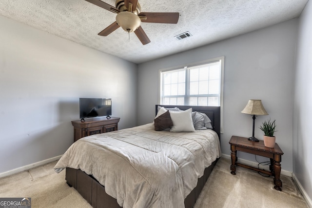 bedroom with visible vents, light carpet, a textured ceiling, baseboards, and ceiling fan