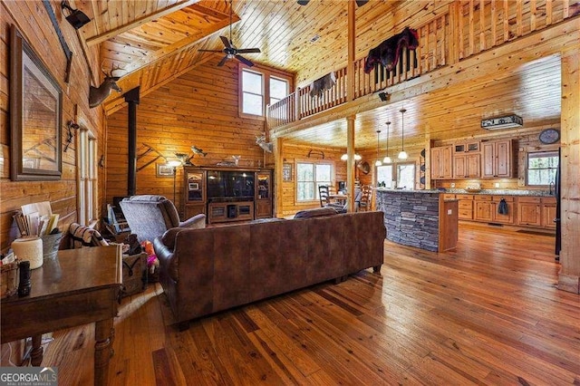 living room with a ceiling fan, hardwood / wood-style flooring, wooden walls, wooden ceiling, and a wood stove