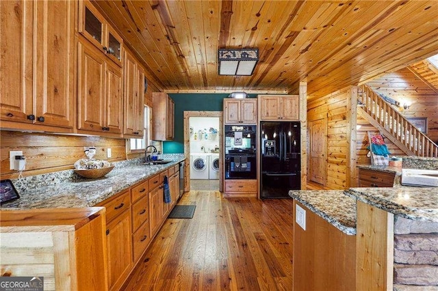 kitchen with a sink, washing machine and dryer, light stone counters, black appliances, and wood-type flooring