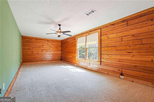 carpeted spare room featuring visible vents, wood walls, a textured ceiling, and a ceiling fan