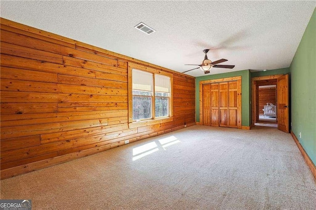 unfurnished bedroom with light colored carpet, visible vents, wood walls, and a textured ceiling